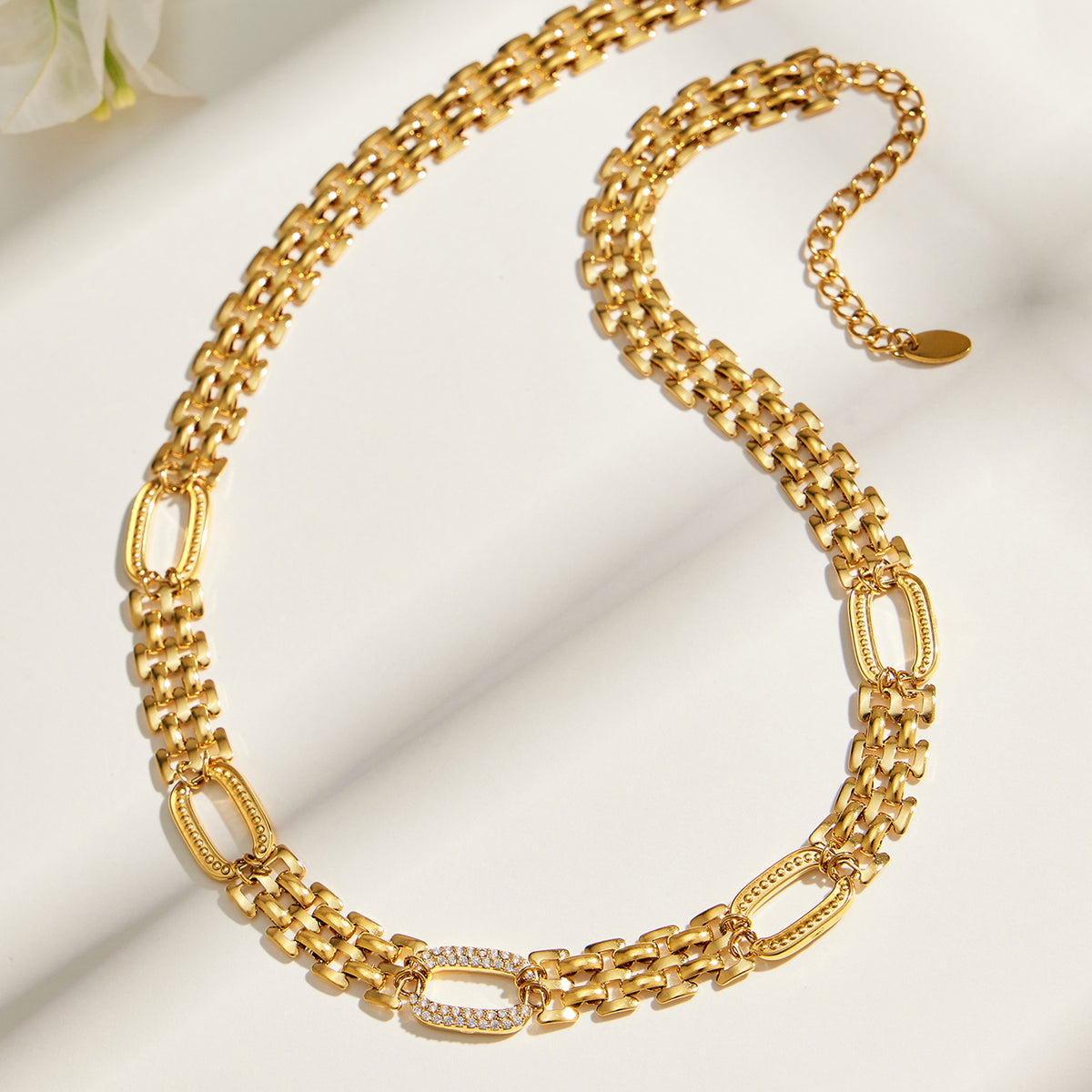 Gold-tone watch link necklace flat lay with decorative zircon-set oval links