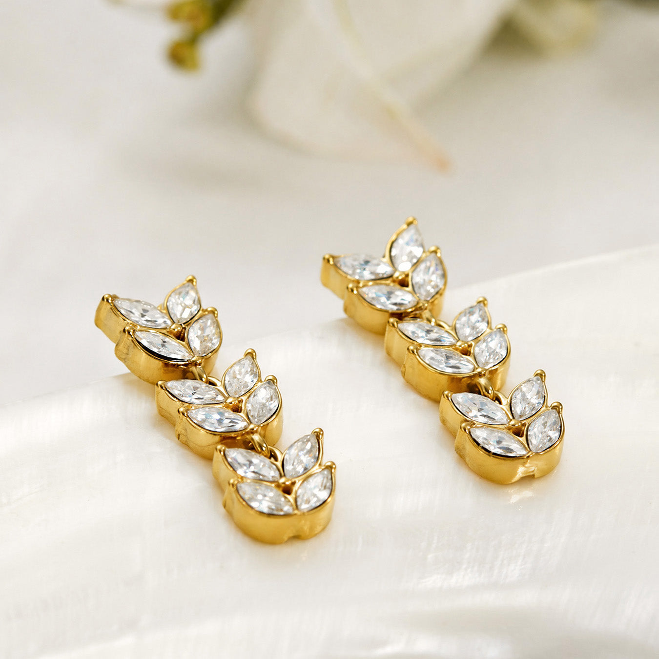 Gold wheat motif drop earrings displayed on a light jewelry background