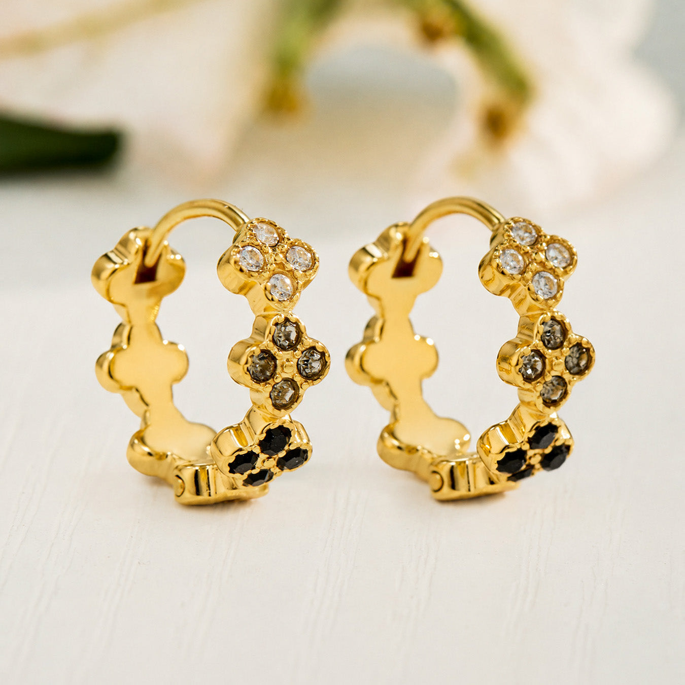 Gold clover huggie earrings displayed with white and black cubic zirconia options