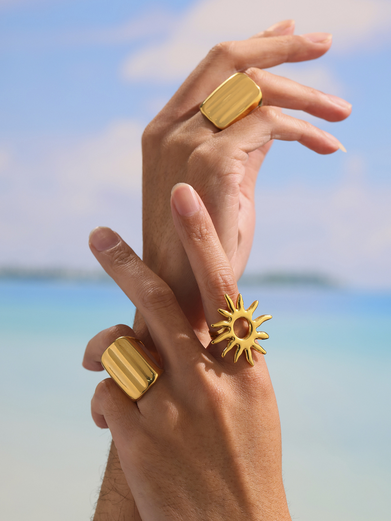 Gold wide band ring and sunburst statement ring worn on hand at the beach