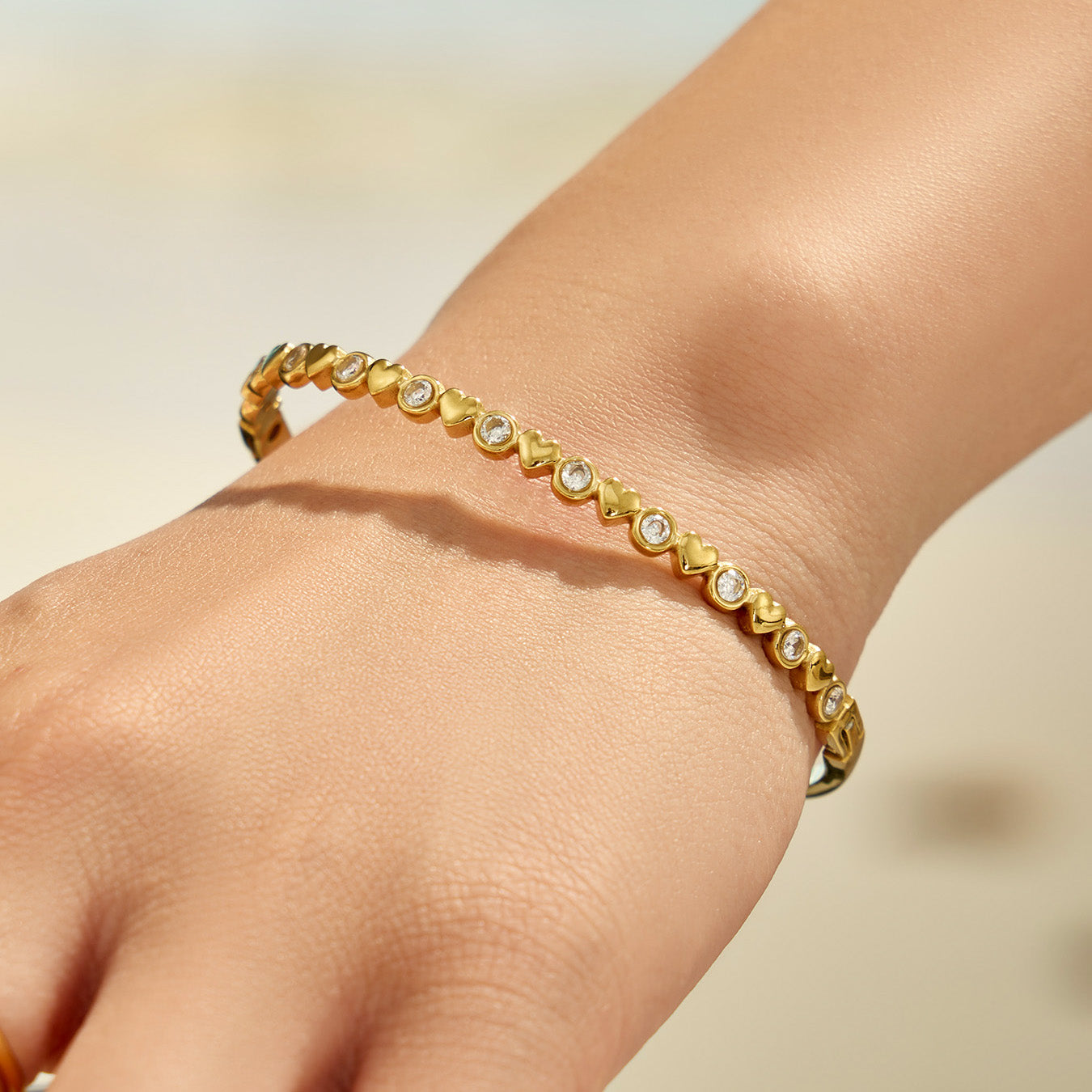 Gold zircon bangle shown on a model hand in natural light