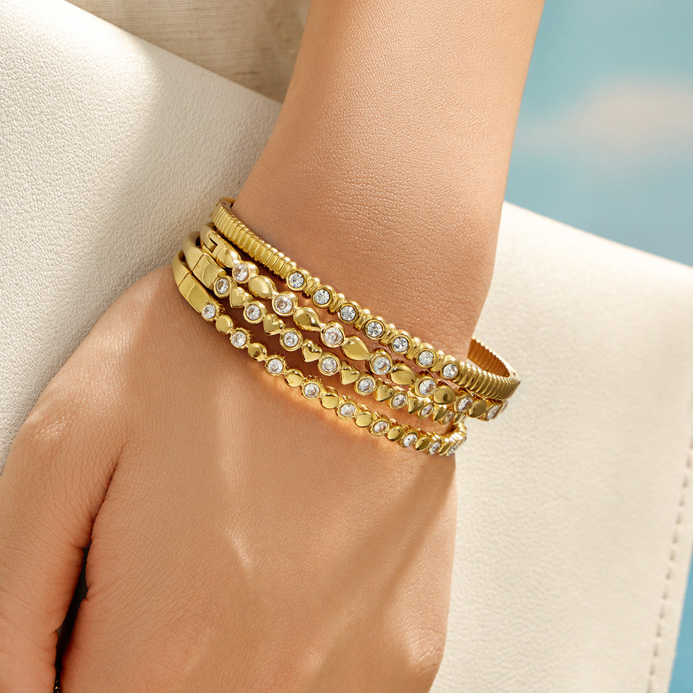 Stacked gold zircon bangles worn on a model wrist near the beach