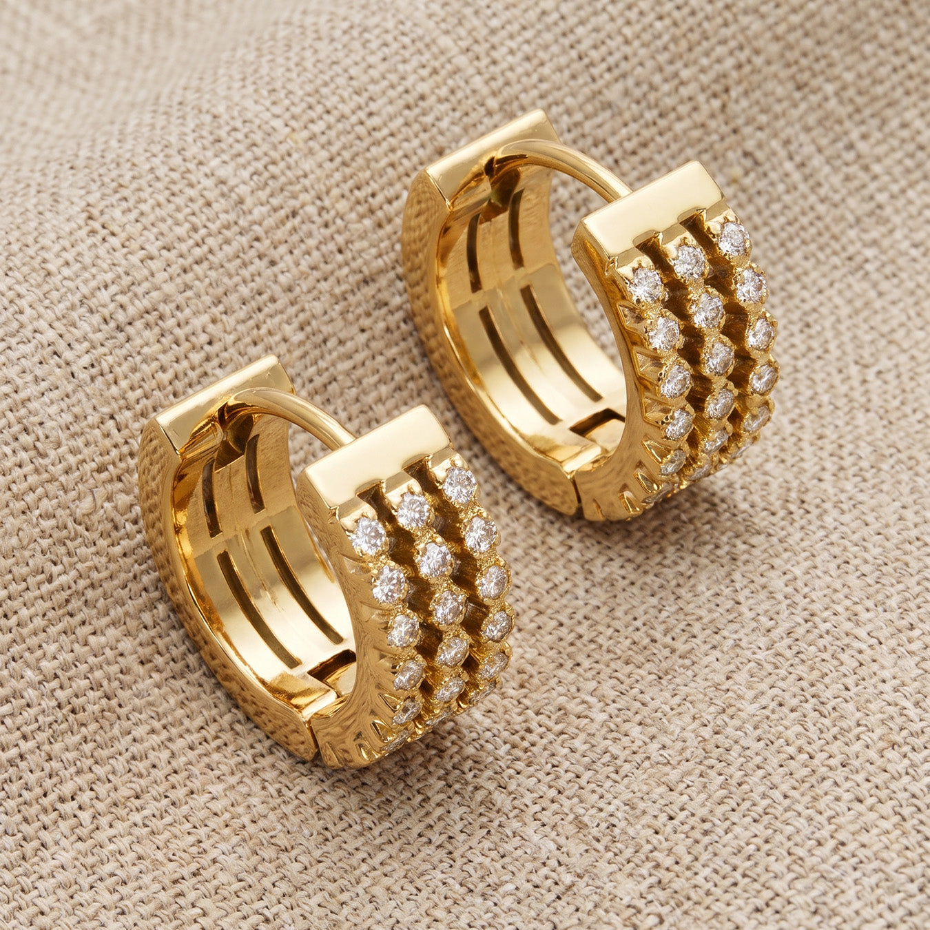 Pair of gold zircon huggie earrings arranged on a warm neutral background