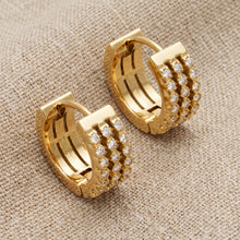 Pair of gold zircon huggie earrings arranged on a warm neutral background