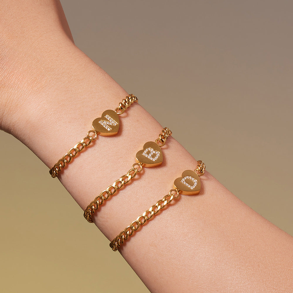 Model wearing two gold-tone zircon initial heart curb chain bracelets on the wrist