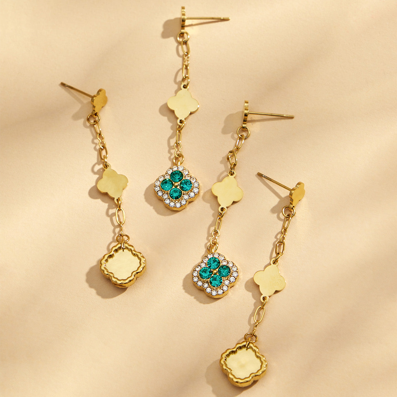 Gold clover drop earrings with green and white crystal details on a beige background