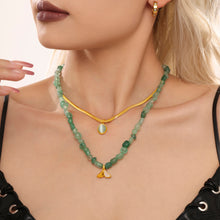 Side view of a model wearing a green bead necklace layered with a gold pendant chain