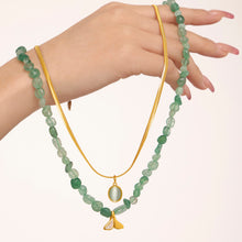 Green beaded and gold chain layered necklaces displayed across a model hand