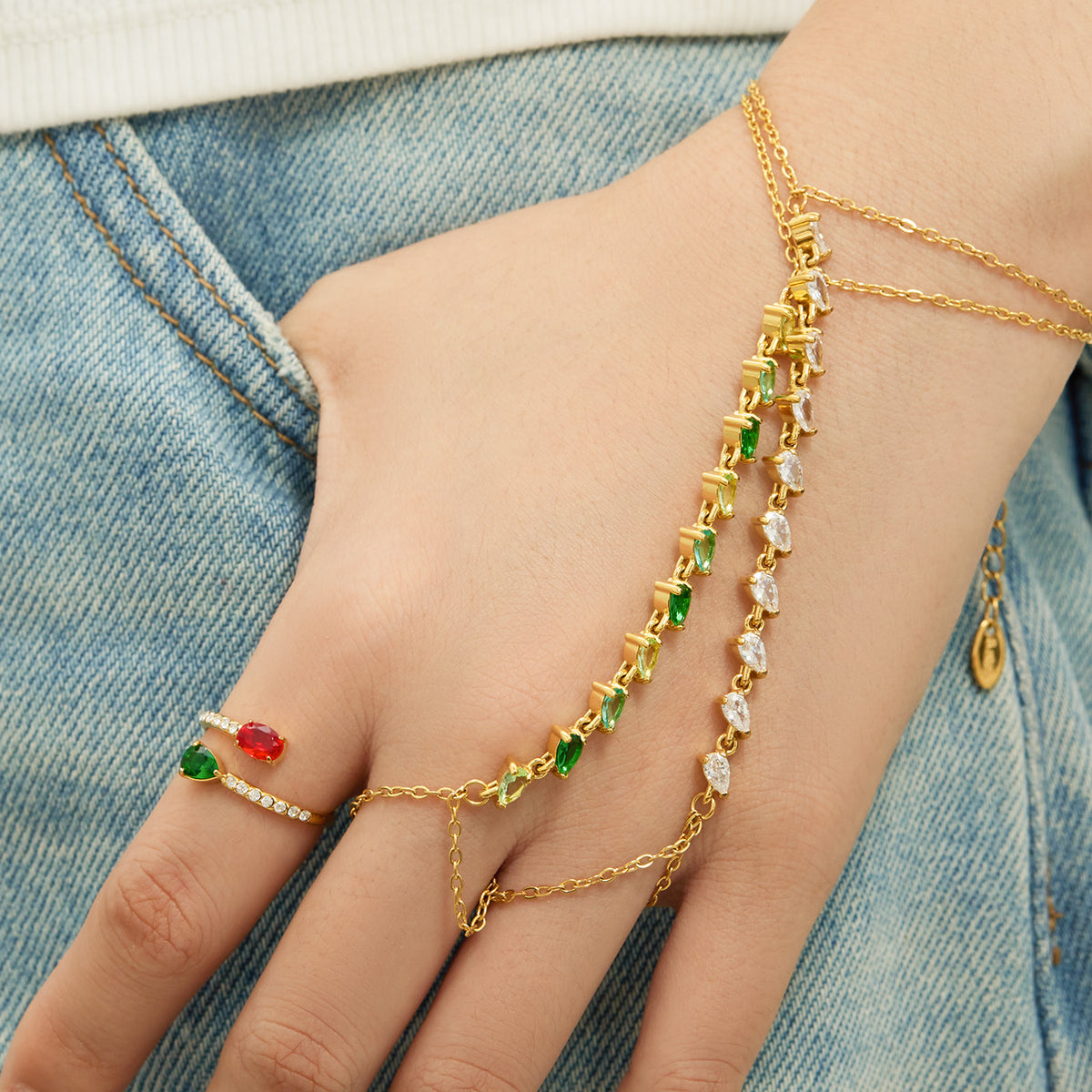 Gold-tone stainless steel hand chain bracelets with green and clear cubic zirconia worn on hand