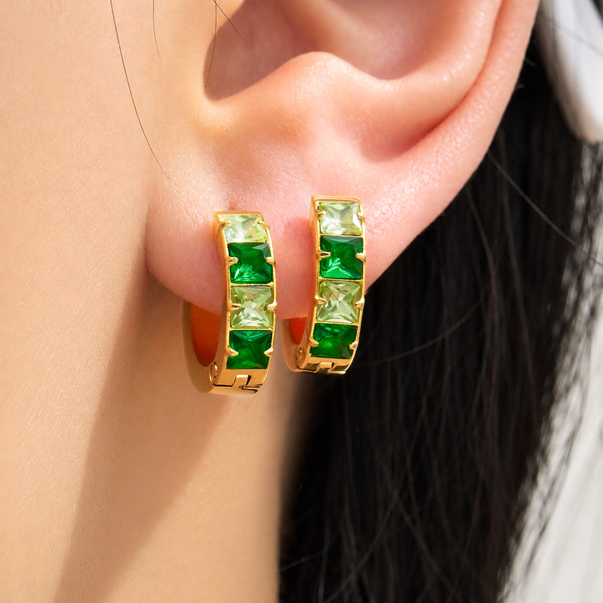 Gold-tone stainless steel huggie earrings with green cubic zirconia worn on ear