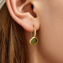 Model wearing green glass stone drop earrings with polished gold-tone setting