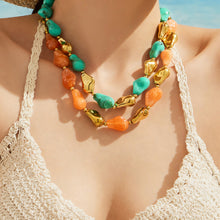 Close-up of model wearing a green and orange chunky resin necklace with organic-shaped beads