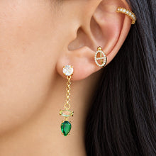 Close-up of a model wearing a gold-tone dangle earring with a vivid green teardrop stone and fine chain links