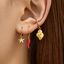 Model wearing gold heart charm huggie earrings with a polished suspended heart pendant