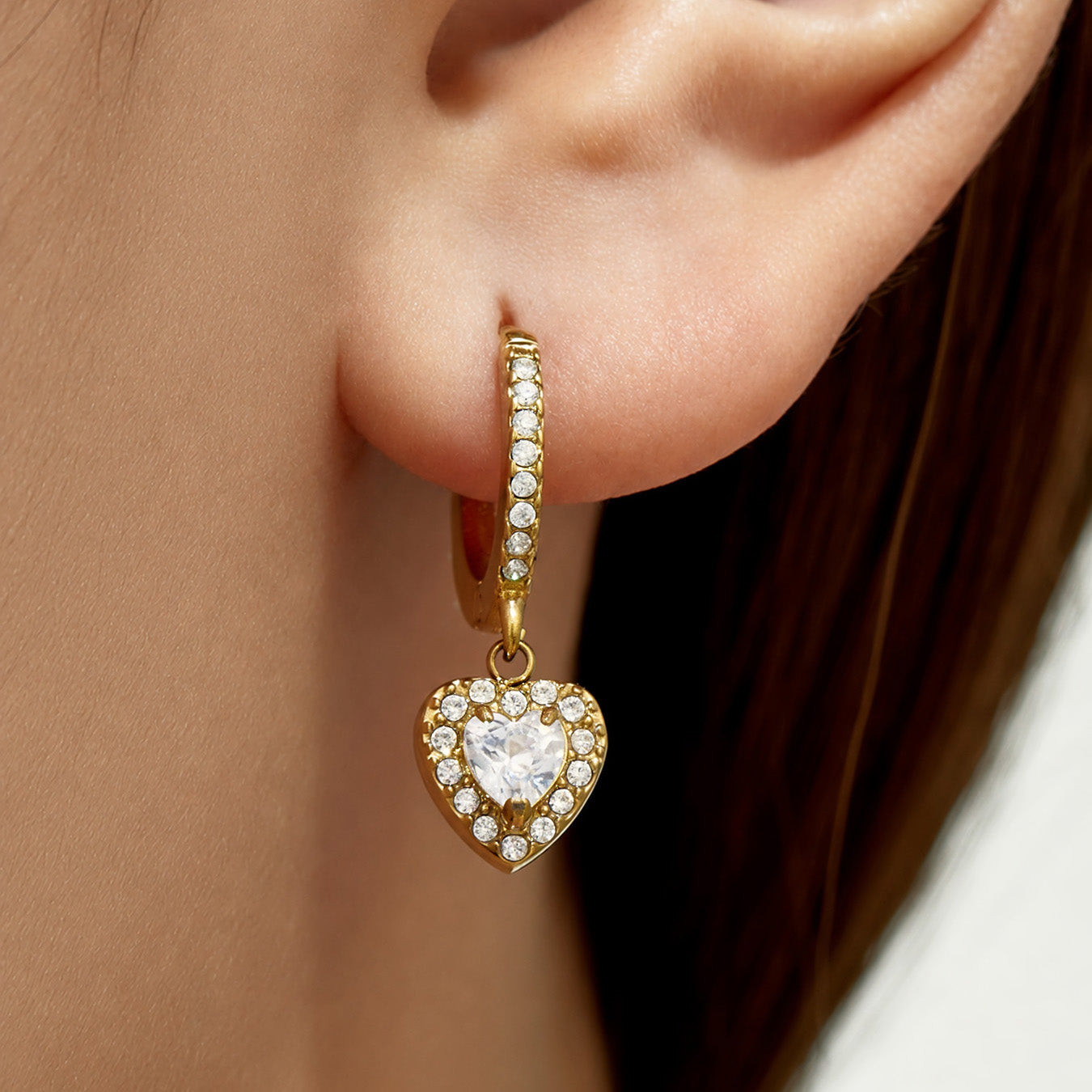 Close-up of gold heart CZ charm huggie earrings with clear cubic zirconia