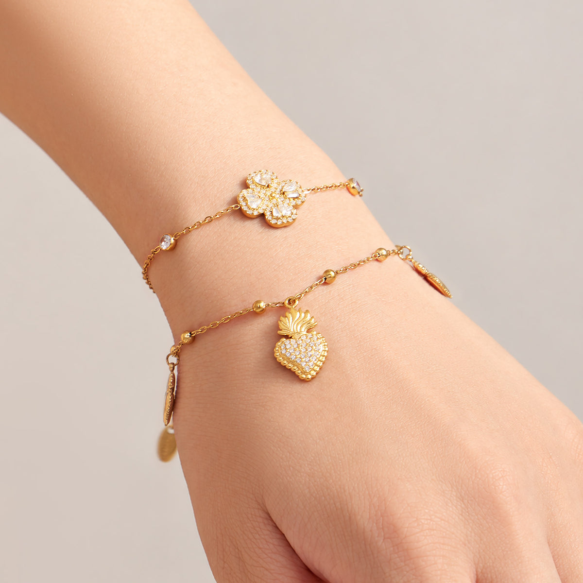 Gold heart zircon charm bracelet and four-petal flower zircon bracelet layered on wrist