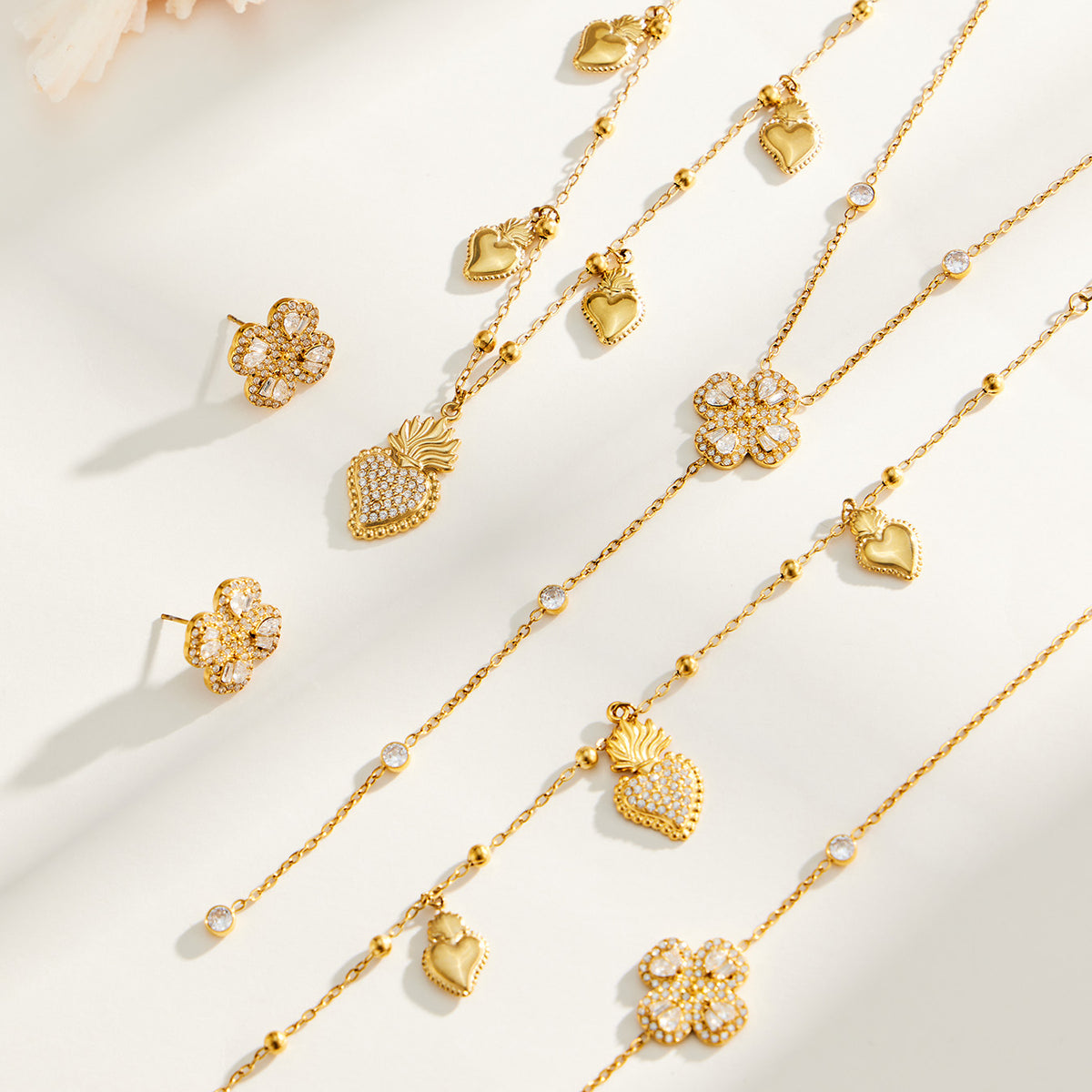 Heart and four-petal flower zircon necklaces, bracelets and earrings displayed in matching gold-tone styles