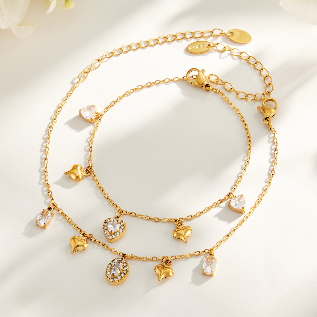 Heart and oval zircon charm bracelets in gold-tone stainless steel displayed together