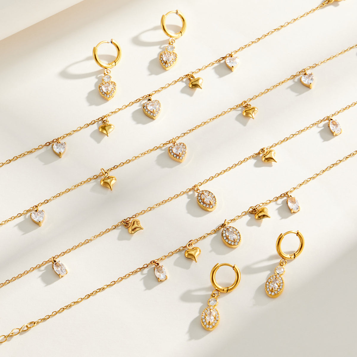 Heart and oval zircon charm necklaces, bracelets and earrings displayed together in gold tone