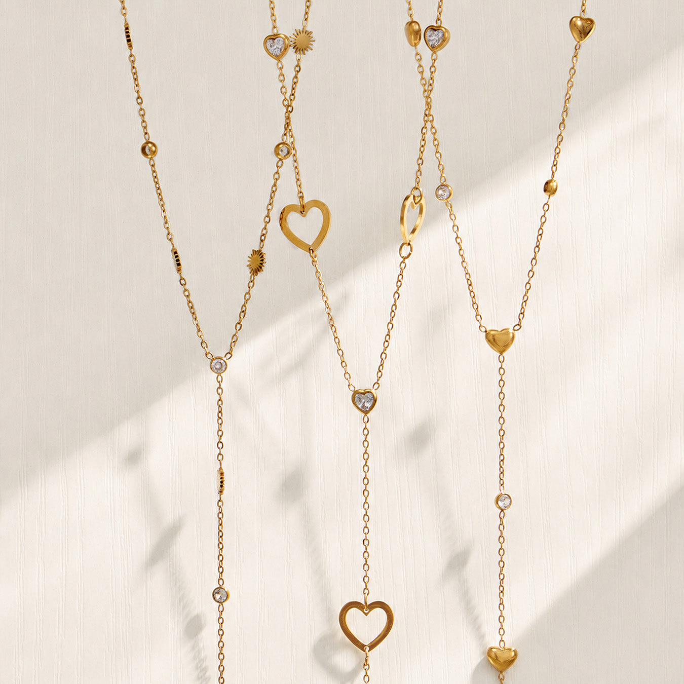 Gold heart and sunflower lariat necklaces displayed together on a light background