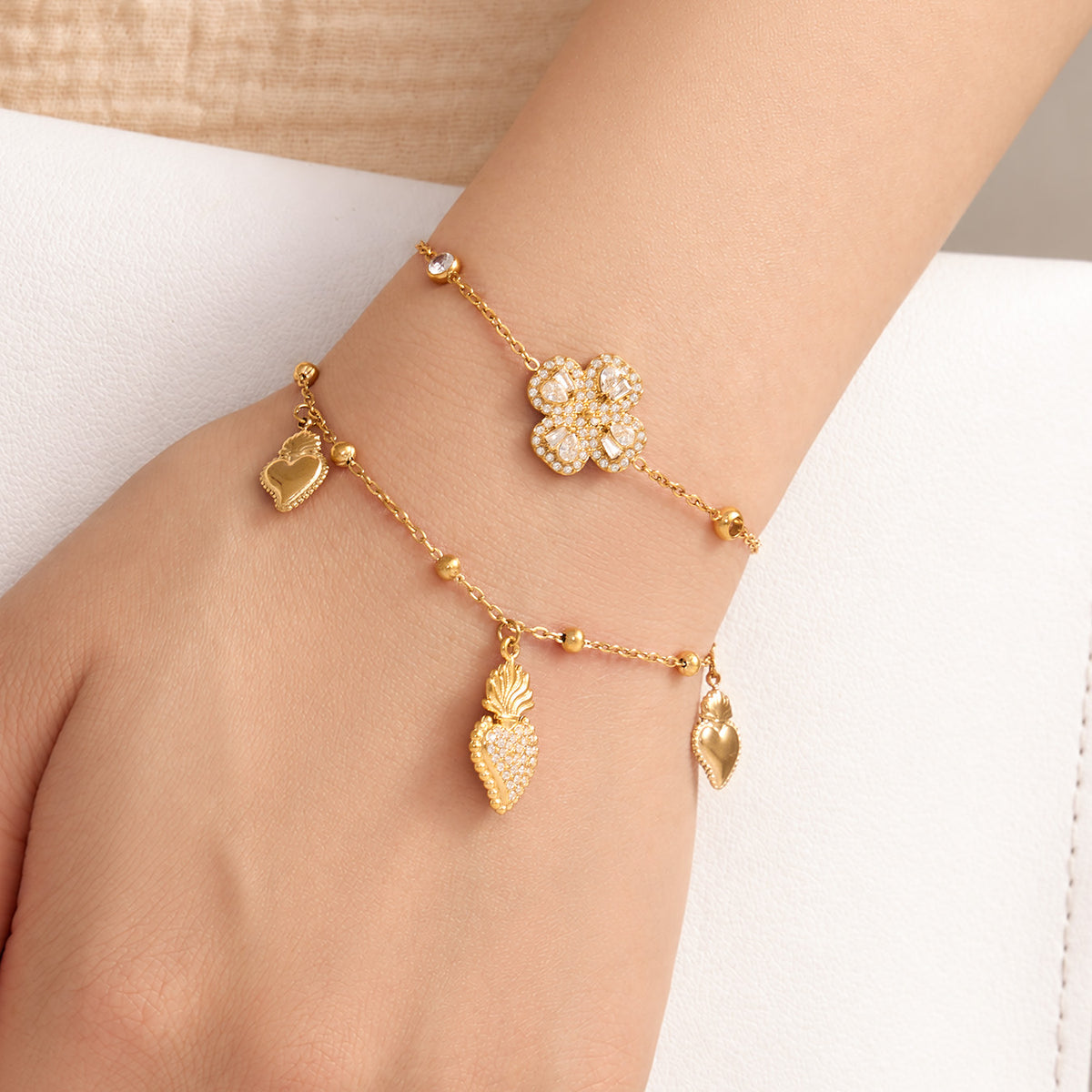 Gold heart zircon charm bracelet with multiple dangling heart accents layered with a flower bracelet on wrist