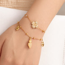 Gold heart zircon charm bracelet with multiple dangling heart accents layered with a flower bracelet on wrist