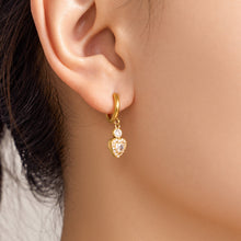 Gold heart zircon hoop earring worn on ear with delicate dangling stone detail