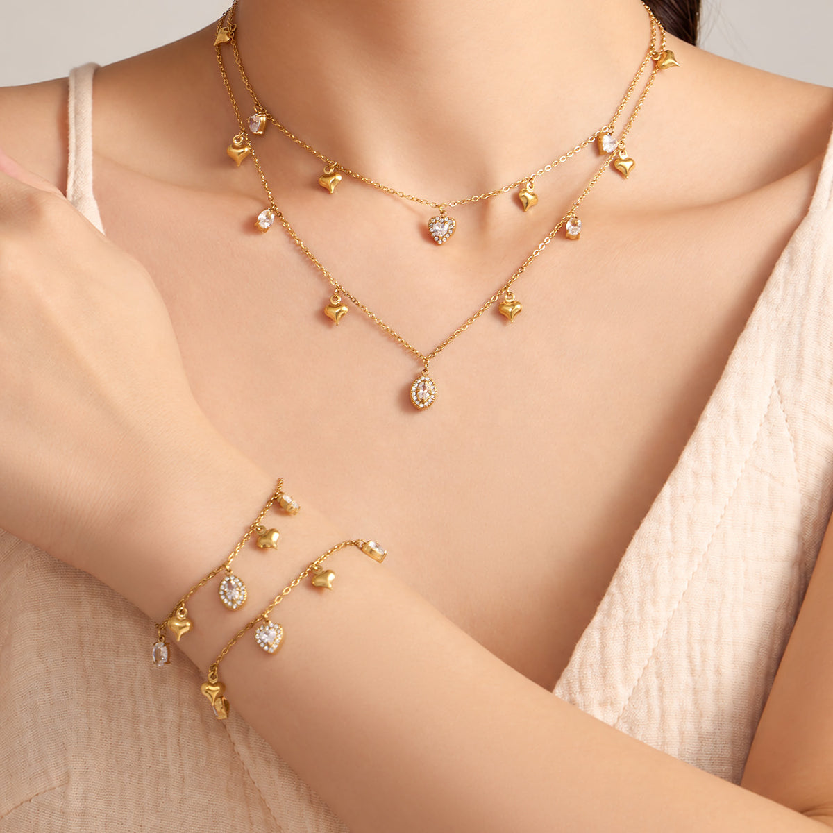 Gold-tone heart and oval zircon charm necklaces and matching bracelets layered on model