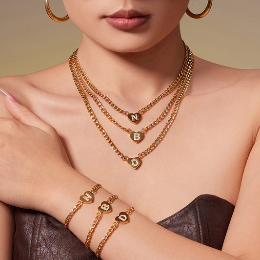 Model wearing layered gold-tone zircon initial heart necklaces with matching curb chain bracelets