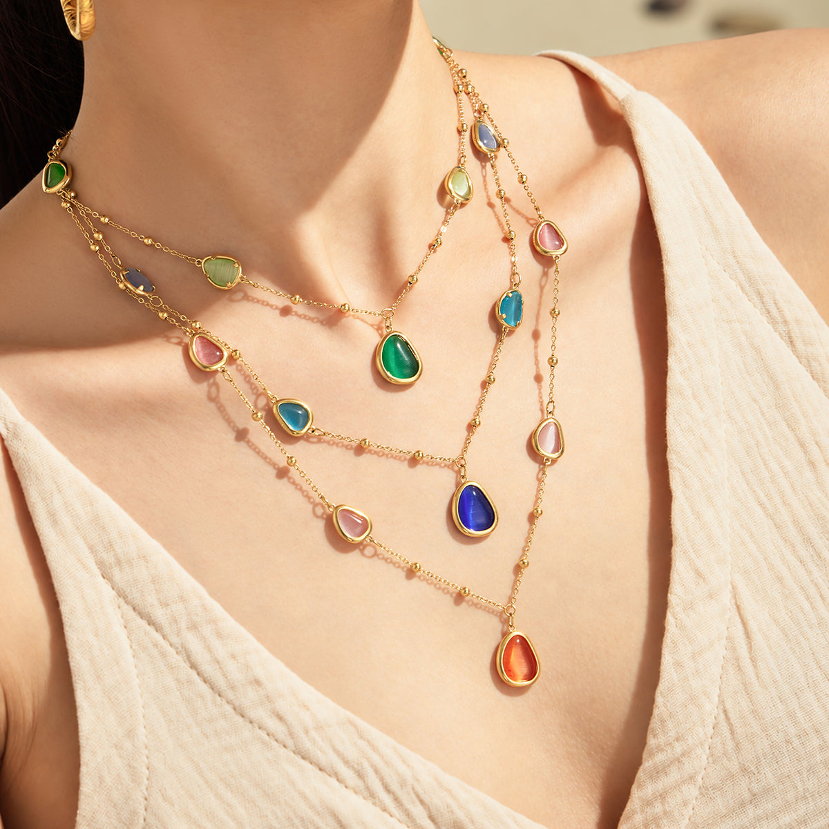Layered gold-tone cat eye necklaces in green, blue and orange worn on model