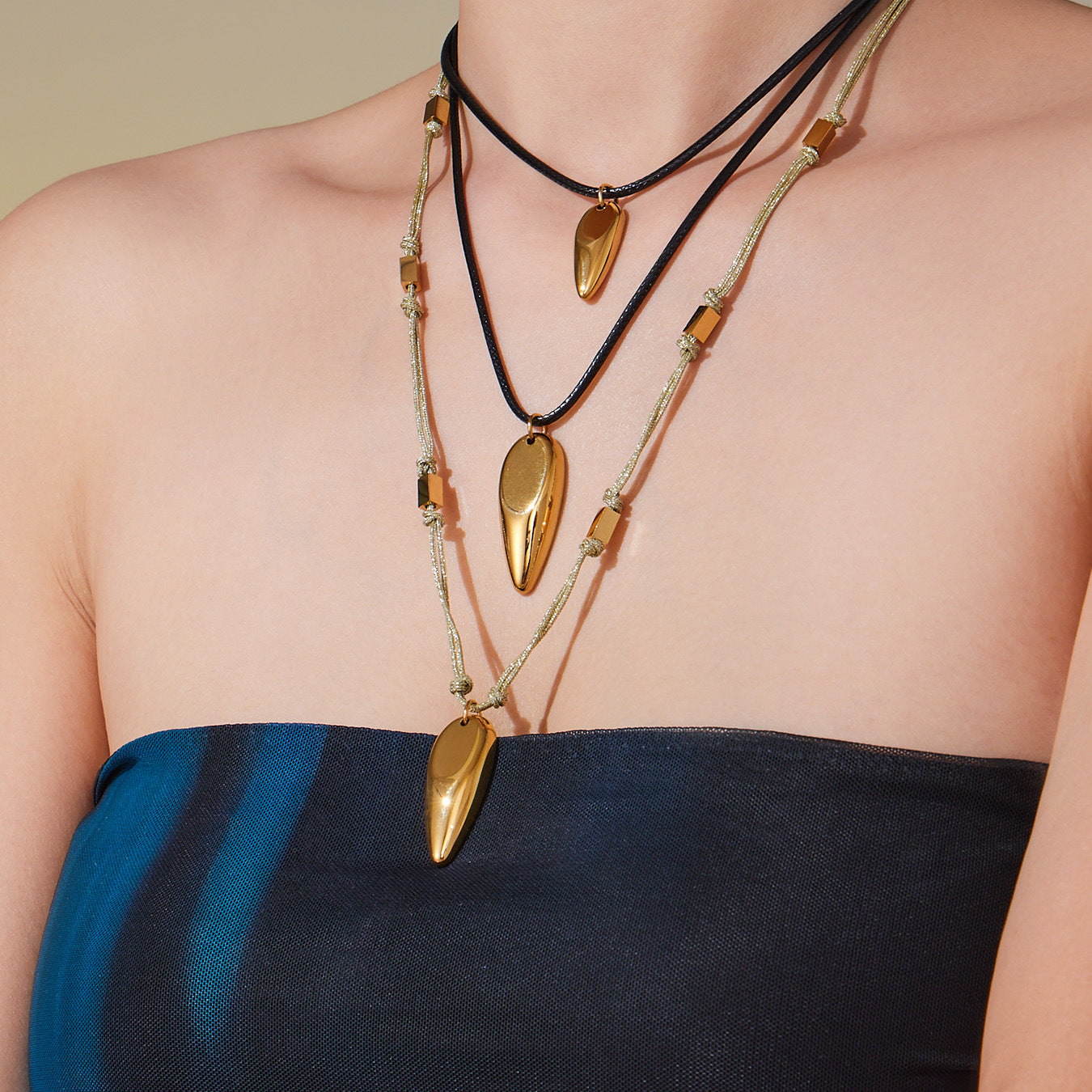 Layered styling photo of teardrop pendant cord necklaces in 316L stainless steel, featuring black leather cord and gold string necklace