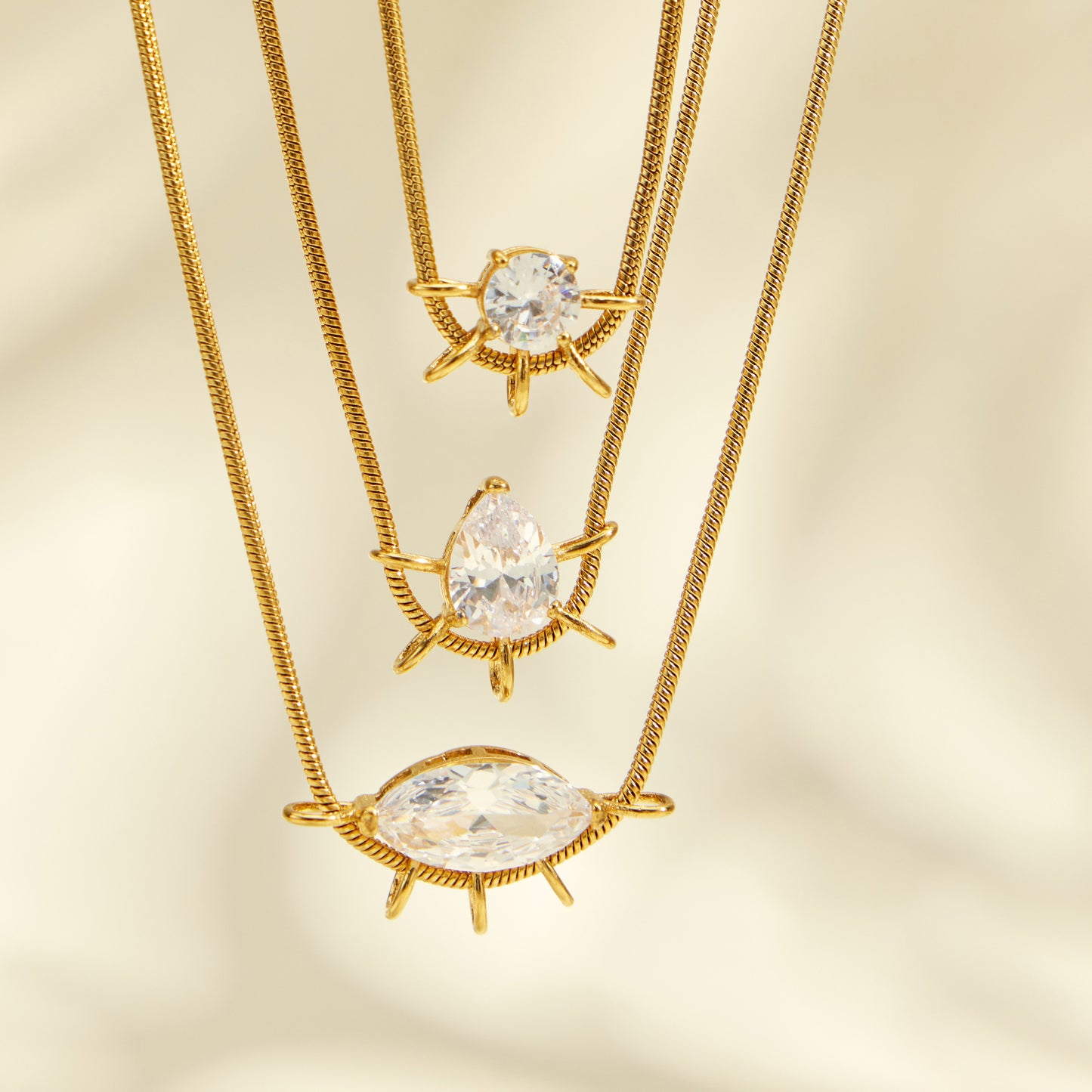 Close-up of round, teardrop and marquise zircon pendants layered on gold-tone chains