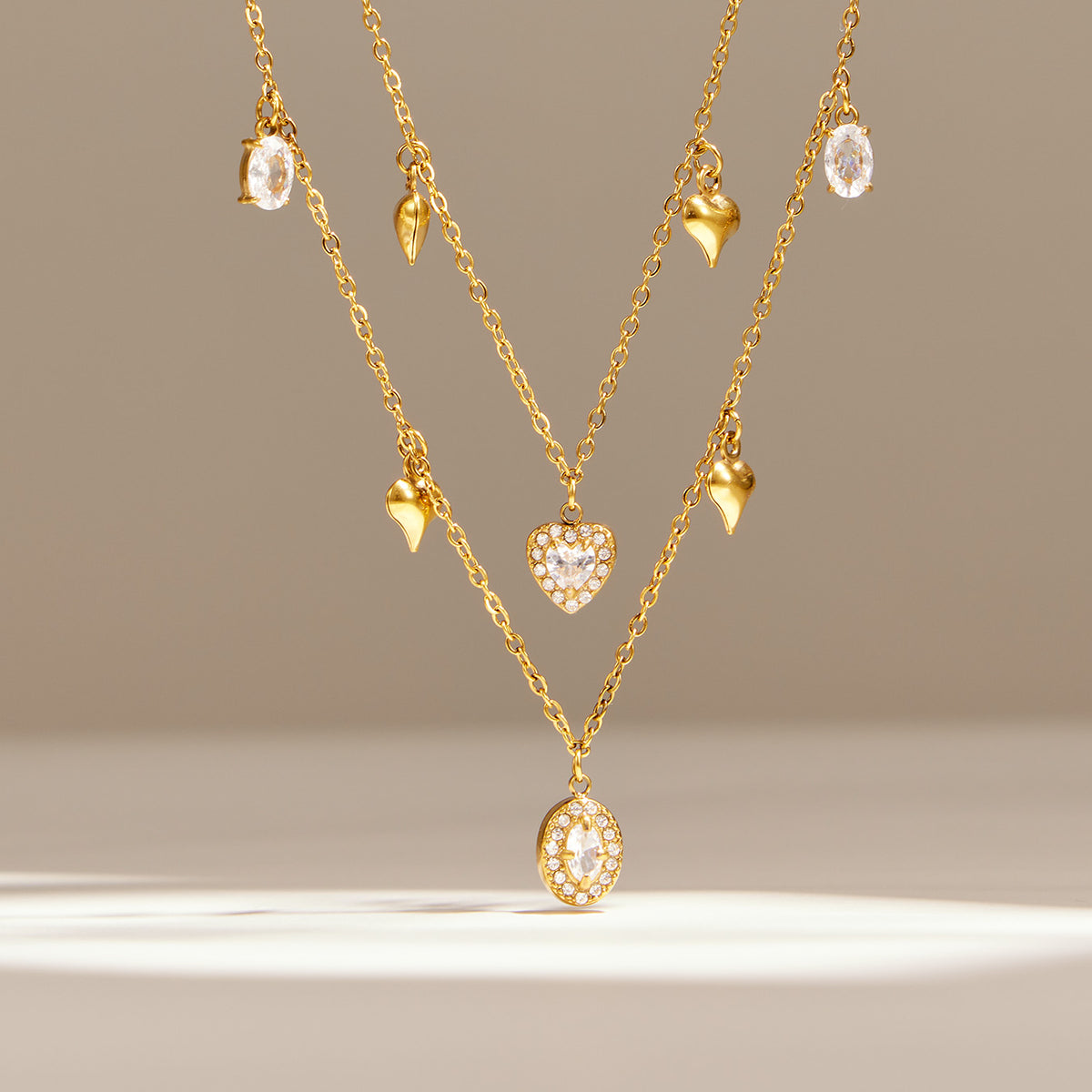 Layered heart and oval zircon charm necklaces in gold tone displayed with matching drop details