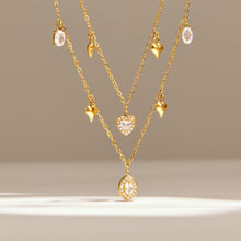 Layered heart and oval zircon charm necklaces in gold tone displayed with matching drop details