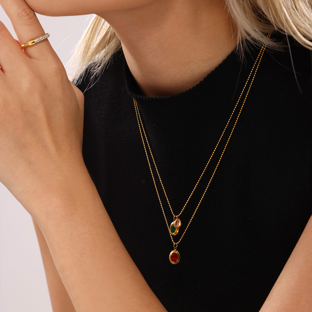 Layered gold necklaces with red zircon pendants styled over a black top
