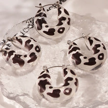 Multiple pairs of black and white leopard print resin hoop earrings arranged in a product display