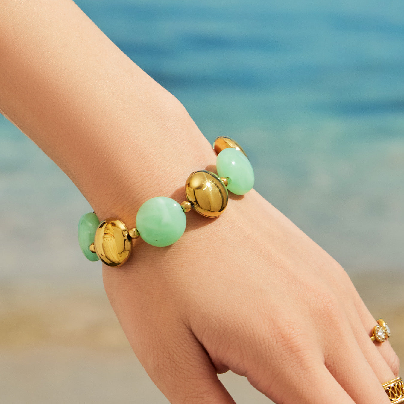 Close-up of a light green resin bead bracelet on the wrist with gold-tone accents.
