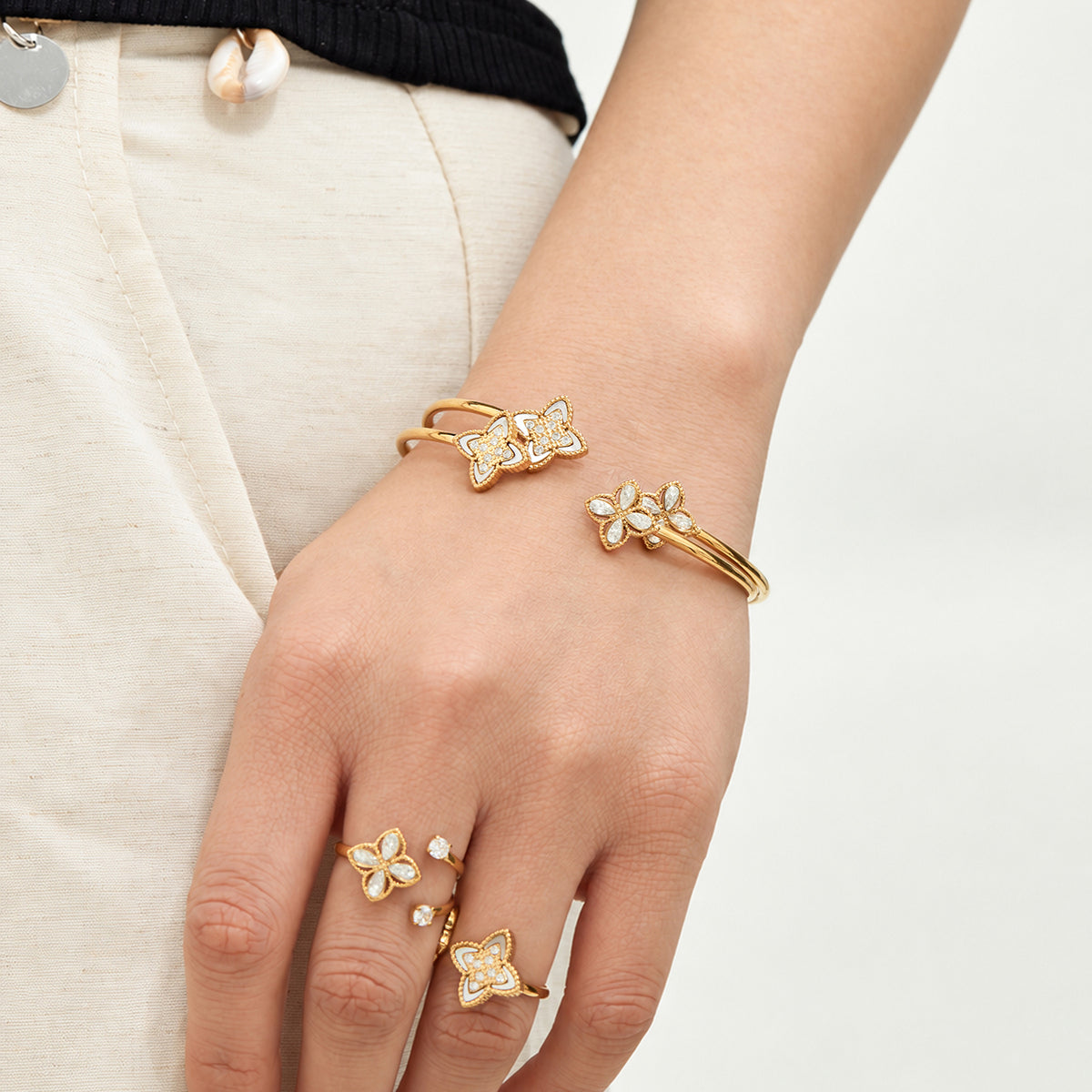 Coordinating gold-tone flower rings and open bangles worn on the hand and wrist