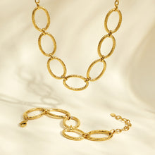 Matching gold oval link necklace and bracelet arranged together on a light background