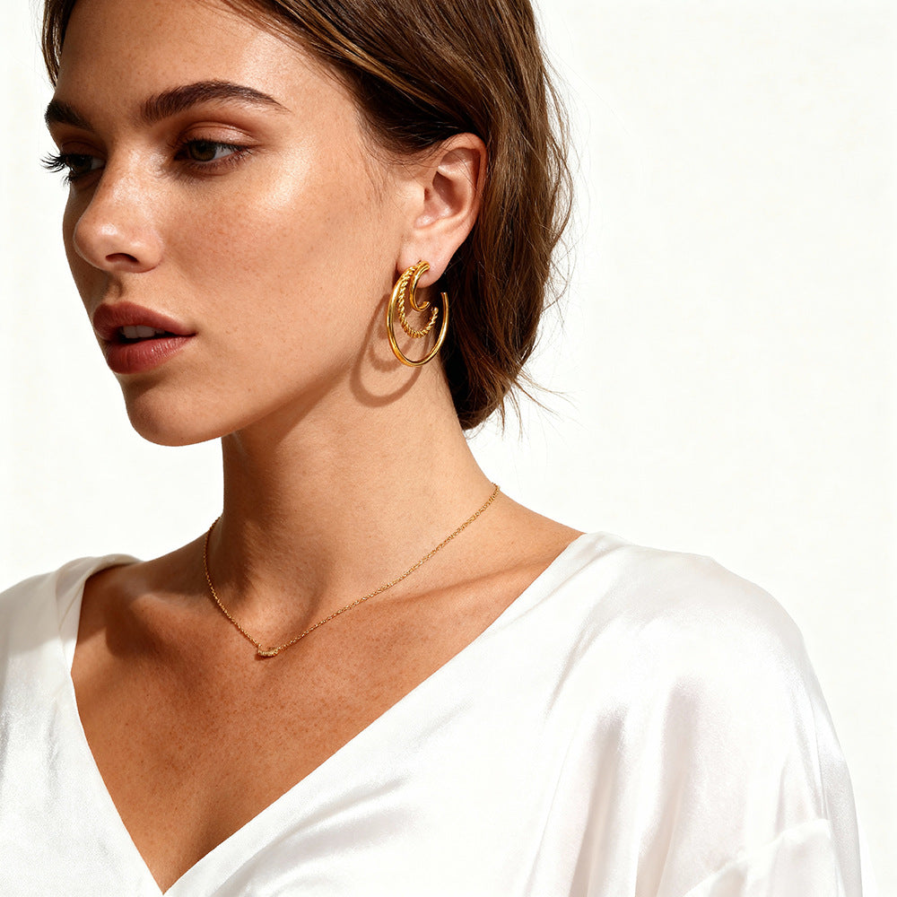 Fashion model styling chunky gold C-hoop earrings with satin white blouse.