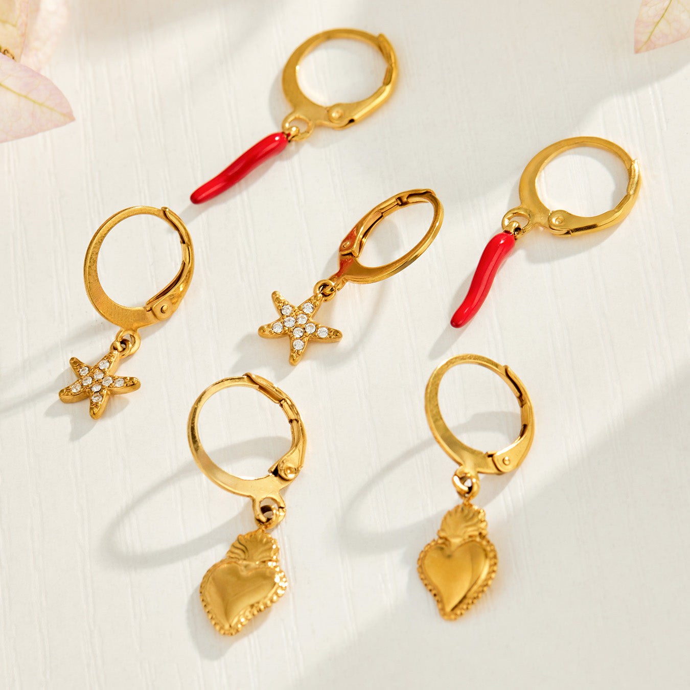 Gold heart, chili pepper and starfish charm huggie earrings arranged together in a flat lay
