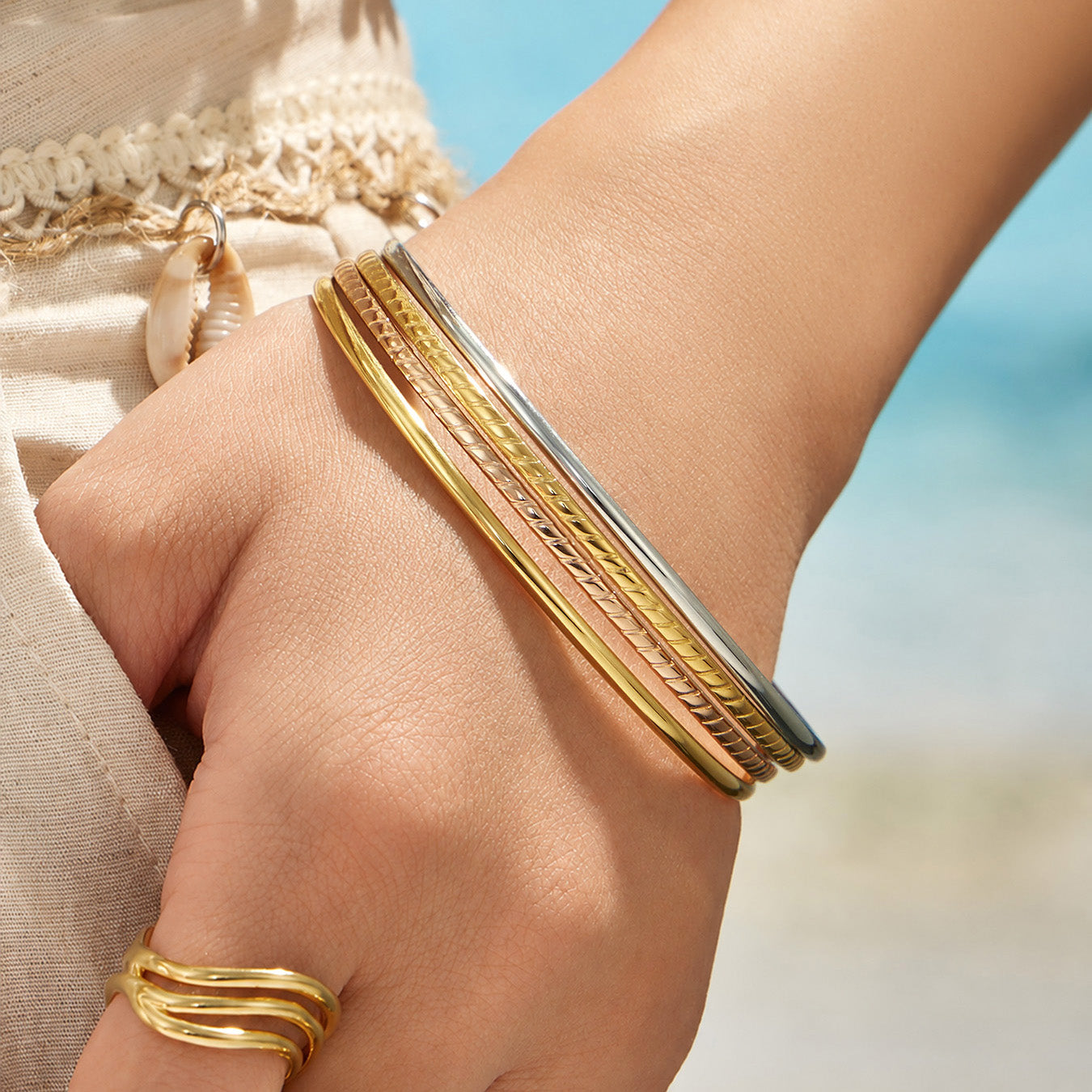 Model wearing layered slim gold and polished steel stackable bangles