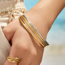 Model wearing layered slim gold and polished steel stackable bangles