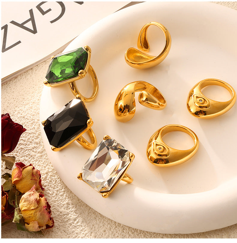 Assorted gold-tone sculptural rings and colored rectangular stone cocktail rings on a white tray