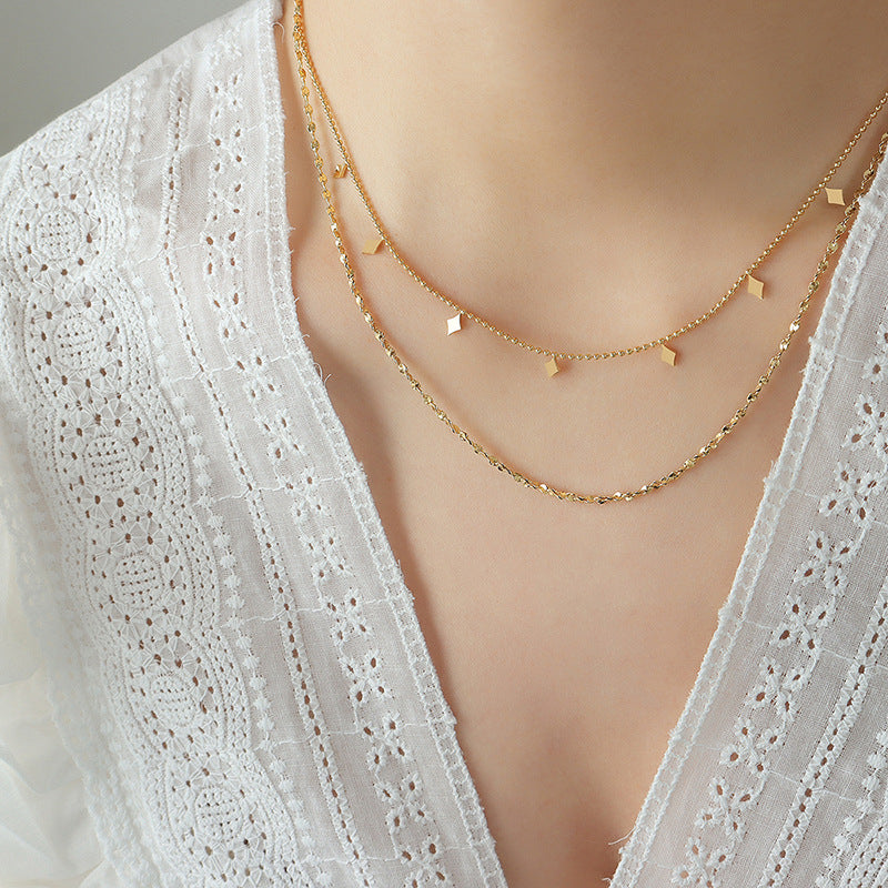 Portrait close-up of a model wearing a gold-tone layered stainless steel necklace with geometric accents