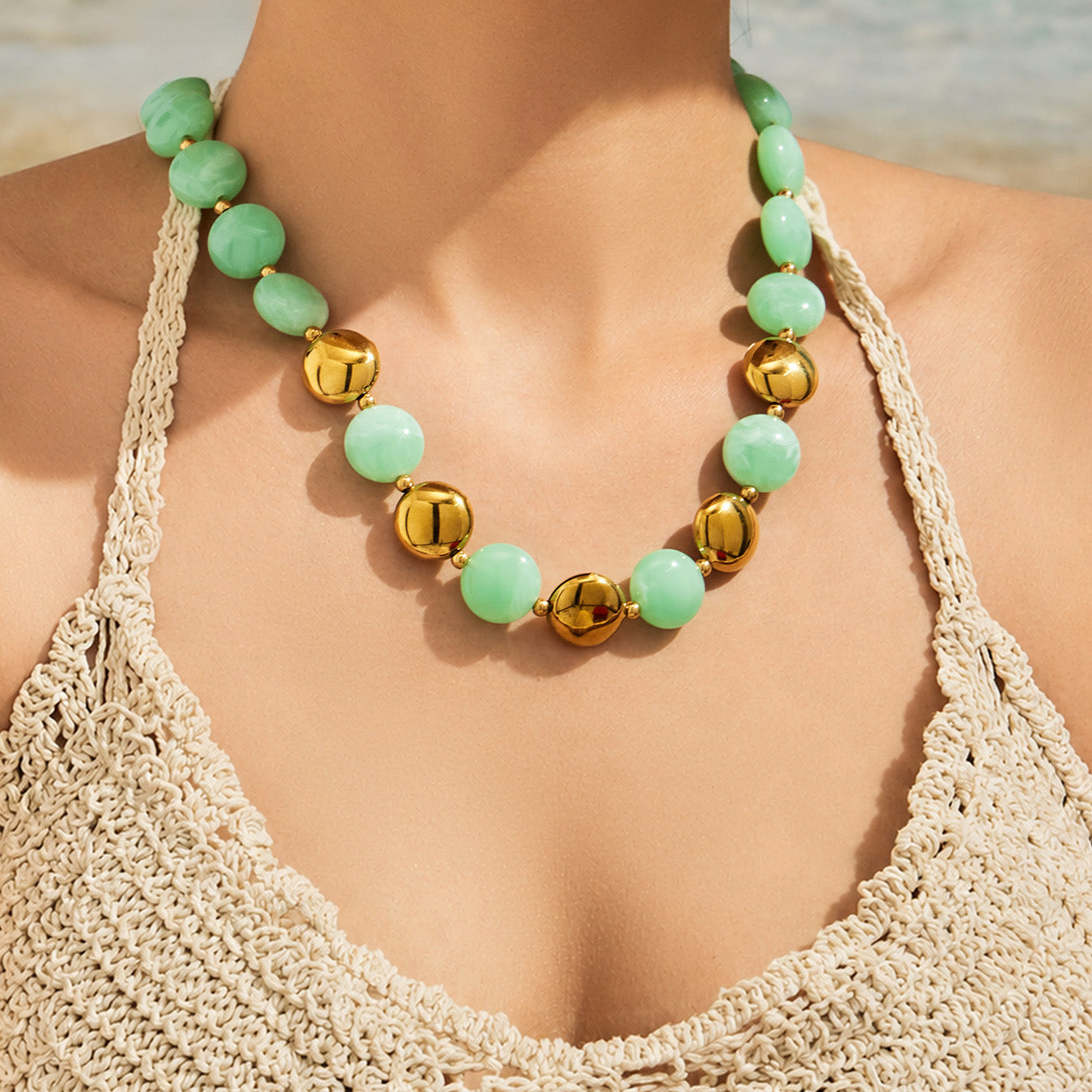 Model wearing a green resin bead necklace with gold-tone accents in a fashionable boutique styling shot.