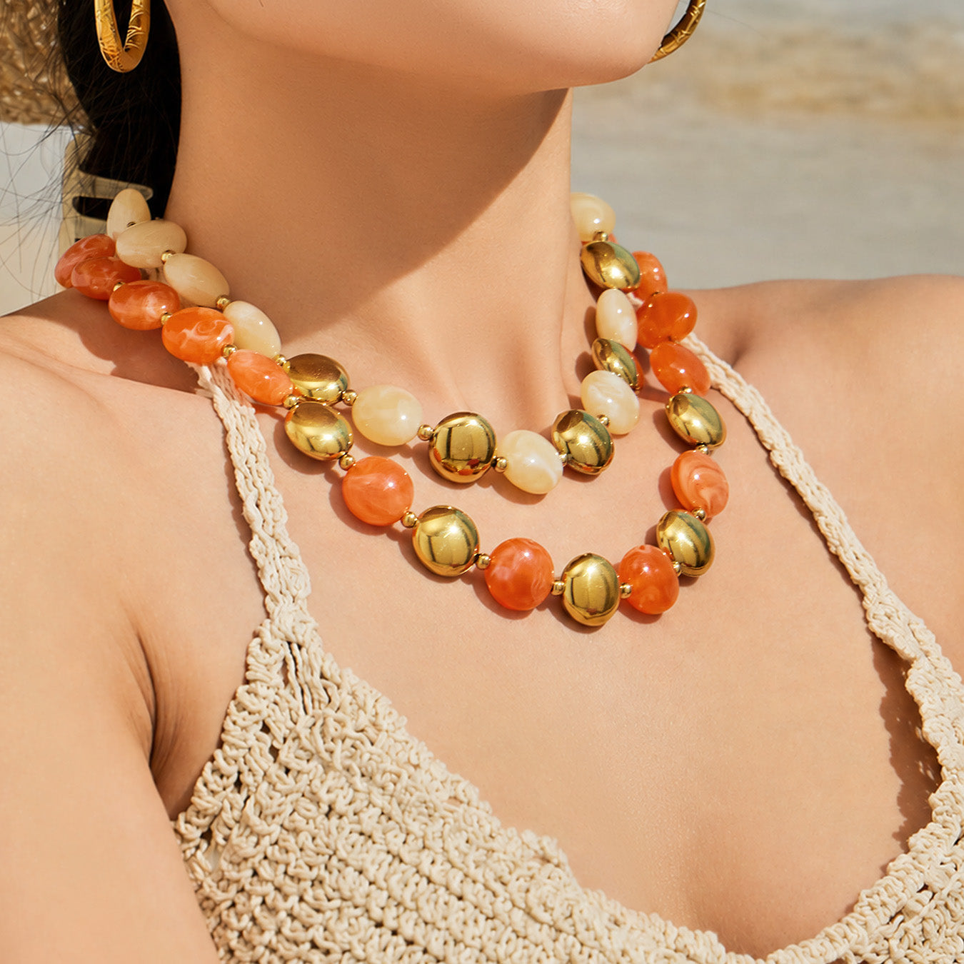 Model wearing an orange-toned resin bead necklace with gold-tone accents in a summer statement jewelry look.