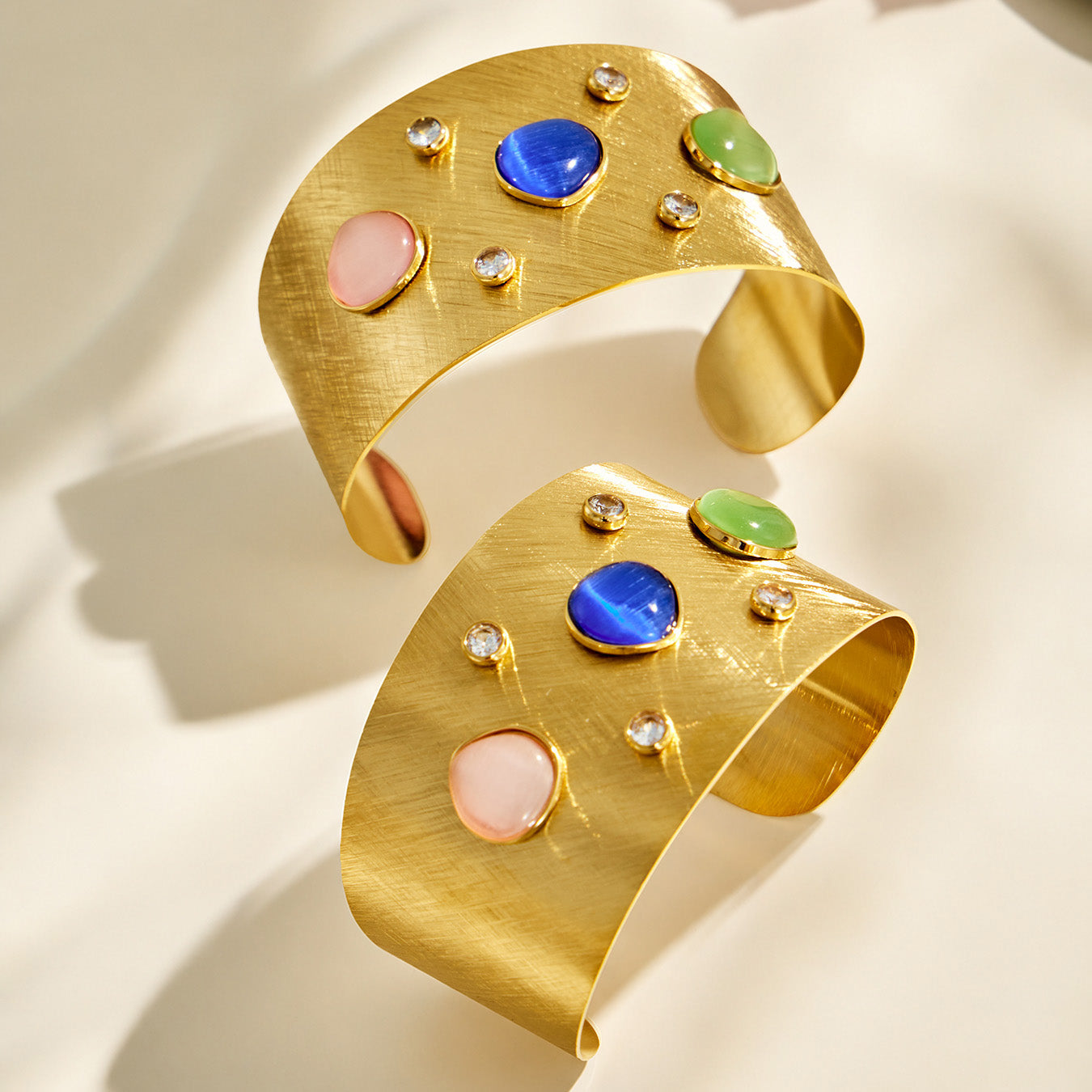 Angled product view of a wide gold open cuff bracelet with multicolor cabochon stones