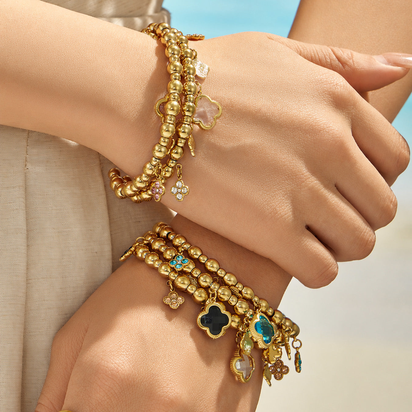 Multicolor four-leaf clover charm bracelets stacked with gold bracelets on a model wrist