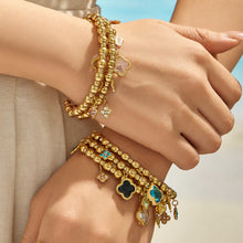Multicolor four-leaf clover charm bracelets stacked with gold bracelets on a model wrist
